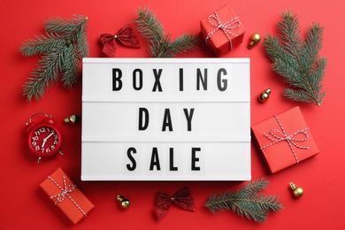Photo of Lightbox with phrase BOXING DAY SALE and Christmas decorations on red background, flat lay