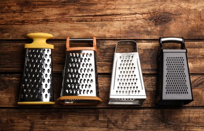 Different modern graters on wooden table, flat lay