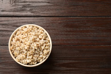 Photo of Delicious pearl barley in bowl on wooden table, top view. Space for text