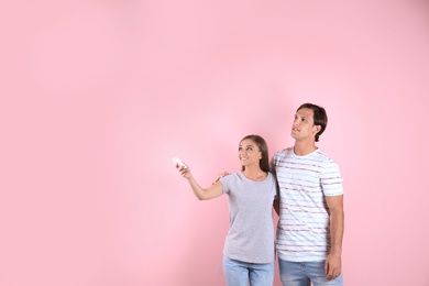 Young couple with air conditioner remote on color background, copy space text