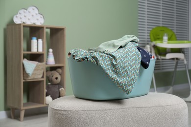 Laundry basket with baby clothes on light ottoman in child room, space for text