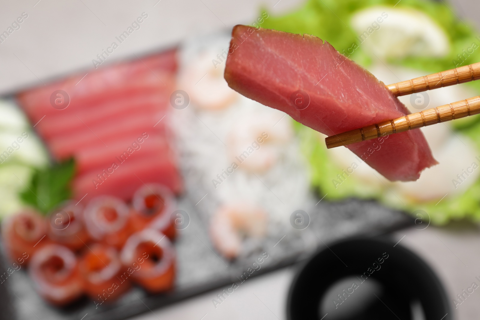 Photo of Chopsticks with tasty sashimi (piece of fresh raw tuna) against blurred background, closeup. Space for text