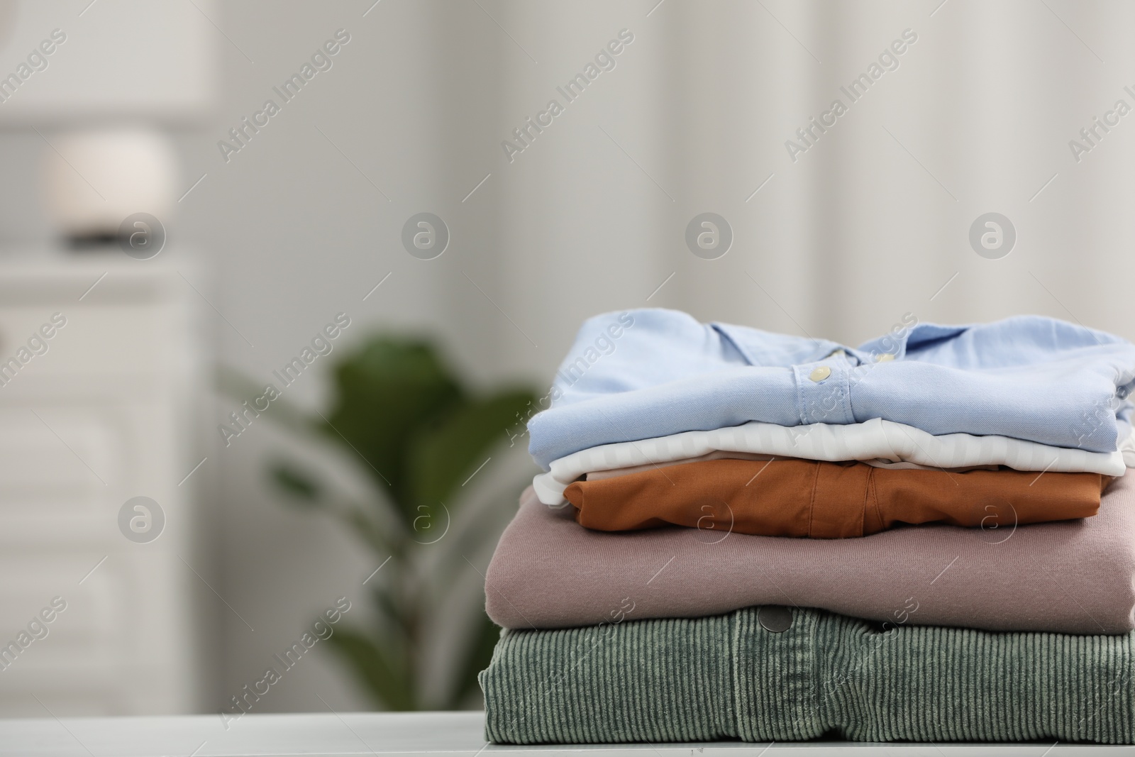 Photo of Stack of different folded clothes on table indoors, closeup. Space for text