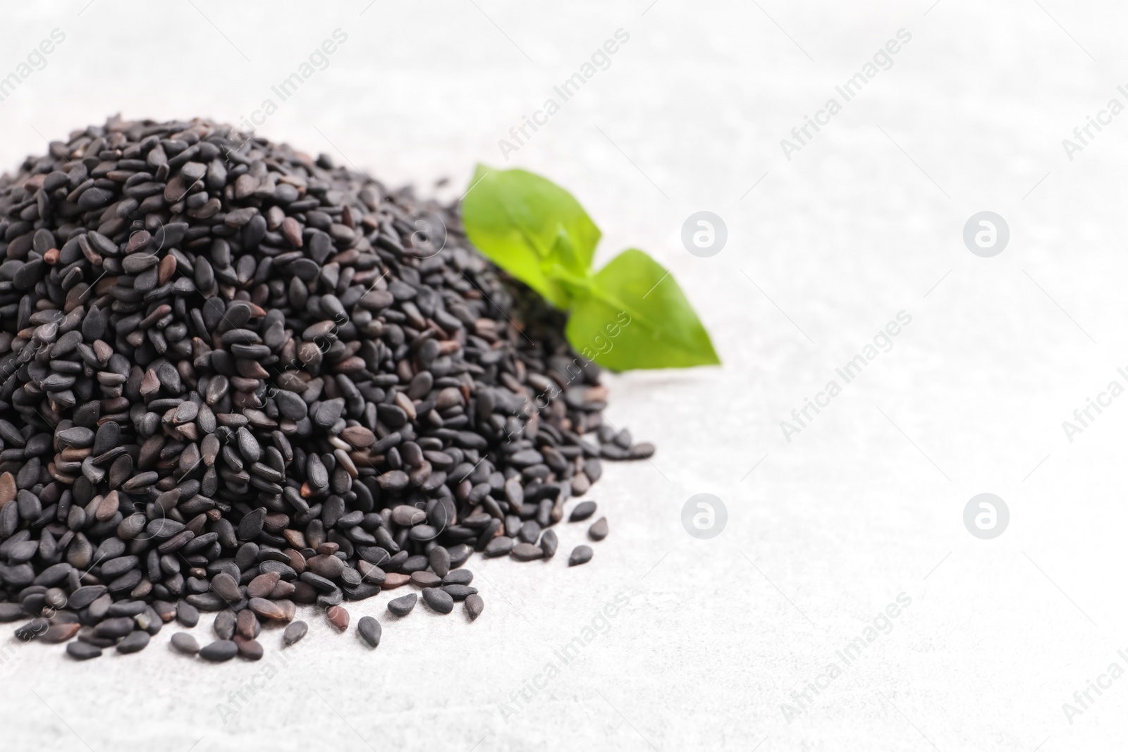 Photo of Pile of black sesame seeds and green leaf on light table, closeup. Space for text