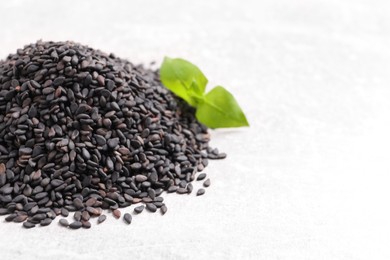 Photo of Pile of black sesame seeds and green leaf on light table, closeup. Space for text