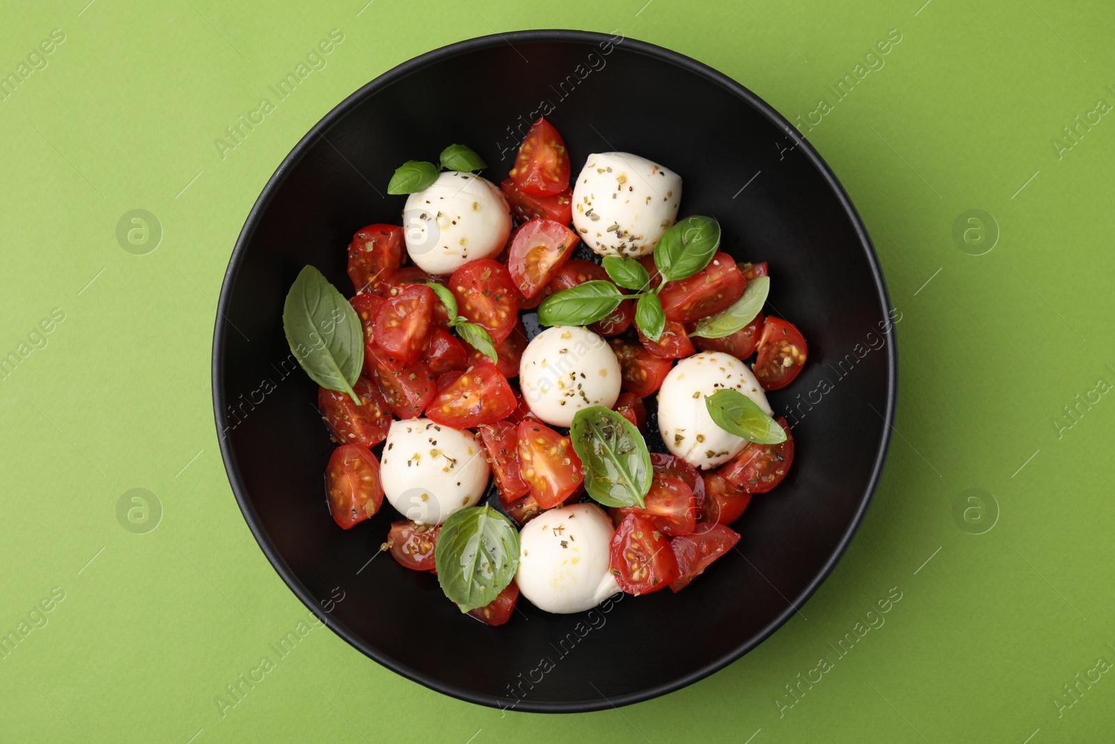 Photo of Tasty salad Caprese with tomatoes, mozzarella balls and basil on green background, top view