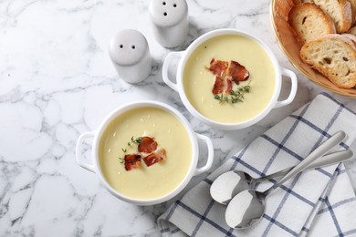 Photo of Tasty potato soup with bacon and rosemary in bowls served on white marble table, flat lay