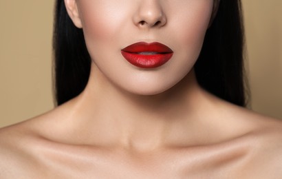 Young woman wearing beautiful red lipstick on beige background, closeup