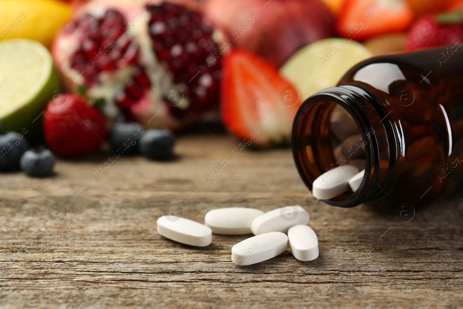 Photo of Vitamin pills, bottle and fresh fruits on wooden table. Space for text