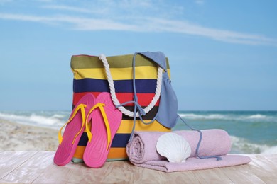 Image of Stylish striped bag and other beach accessories on wooden table near sea