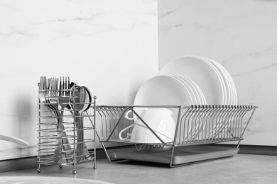 Photo of Drying rack with clean dishes near cutlery holder on table in kitchen