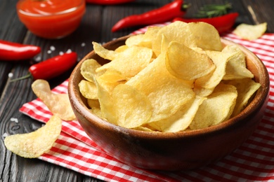 Bowl with potato chips on wooden table, closeup