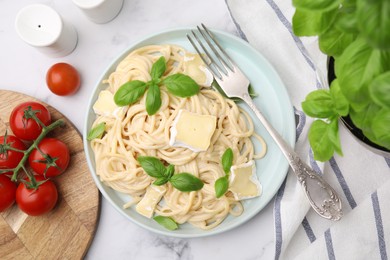 Photo of Delicious pasta with brie cheese, basil and fork on white marble table, flat lay