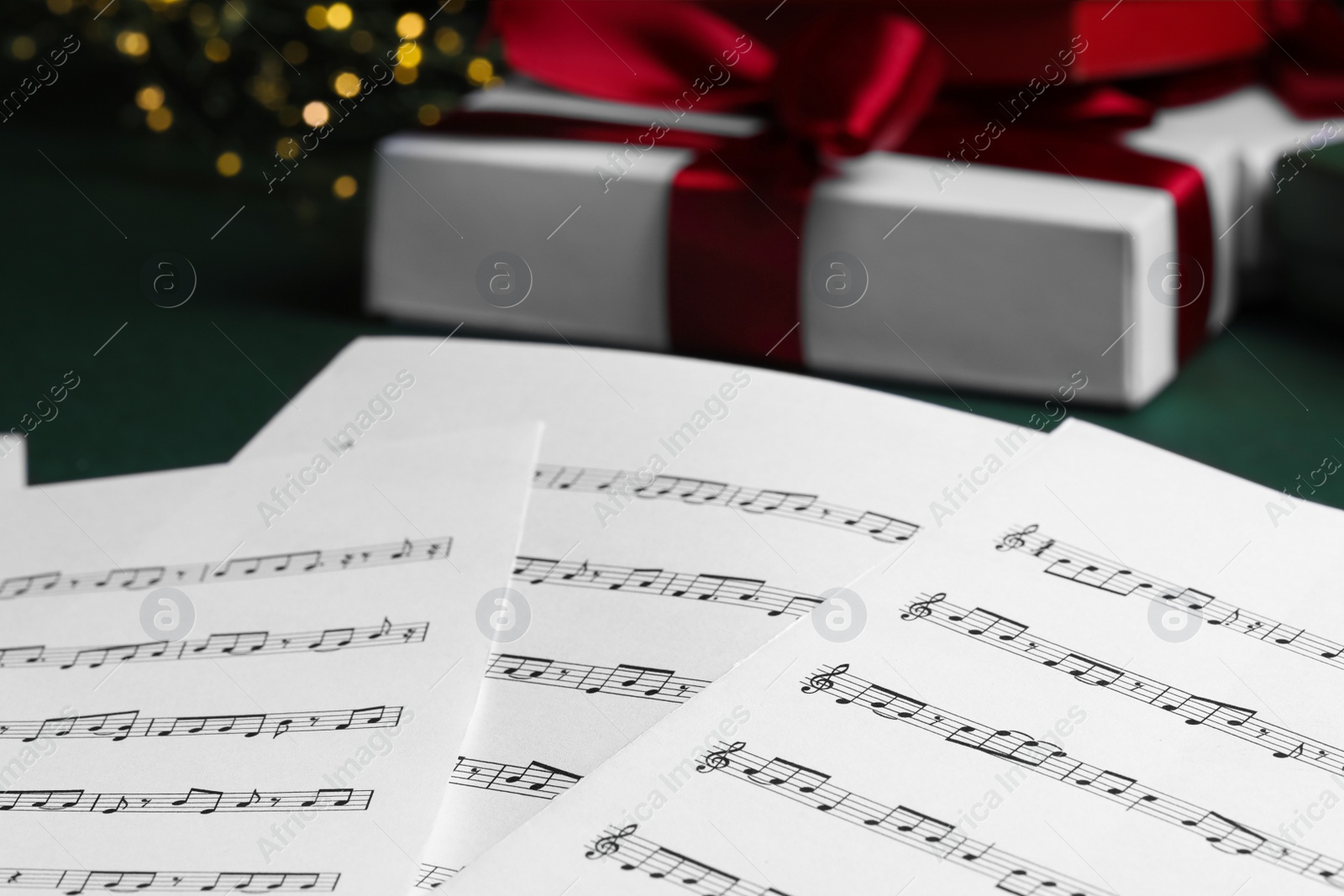 Photo of Note sheets, fairy lights and Christmas gift boxes on green table, closeup