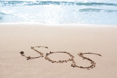 Message SOS drawn on sandy beach near sea