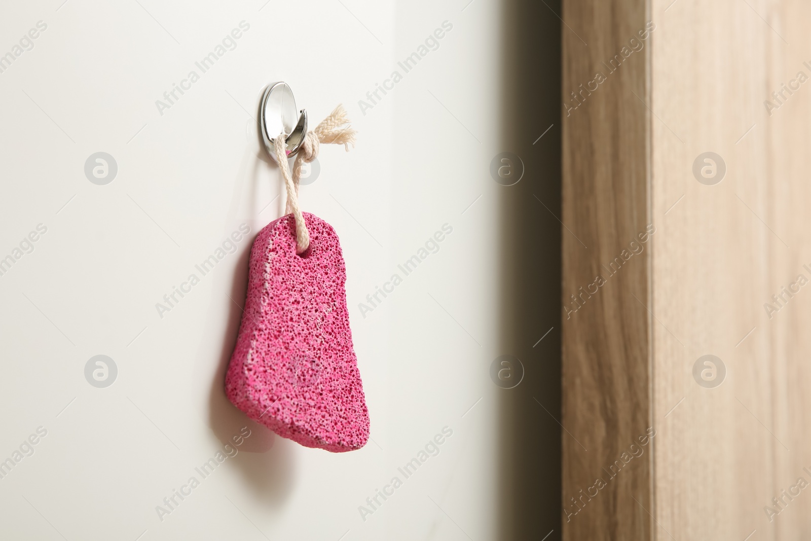 Photo of Pink pumice stone hanging on white wall, space for text