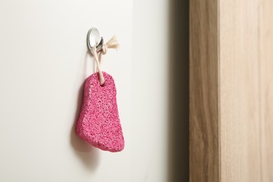Photo of Pink pumice stone hanging on white wall, space for text
