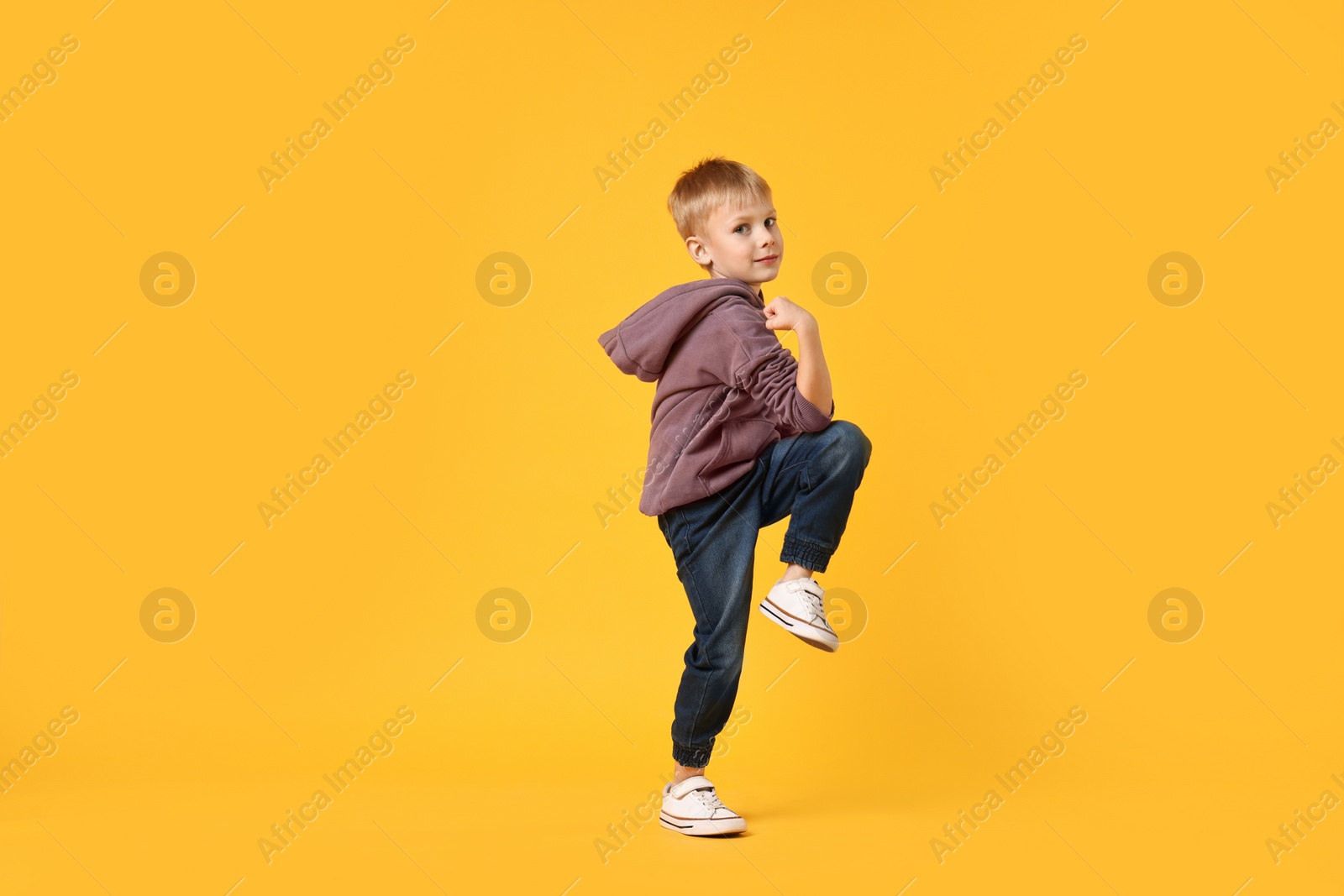 Photo of Happy little boy dancing on yellow background. Space for text