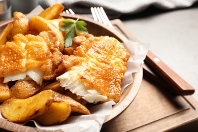 Photo of Wooden plate with British traditional fish and potato chips on table, closeup