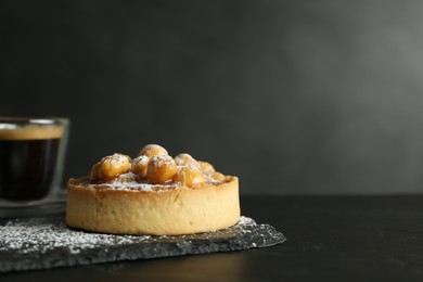 Photo of Delicious tart with hazelnuts, sweet caramel and powdered sugar on black table. Space for text
