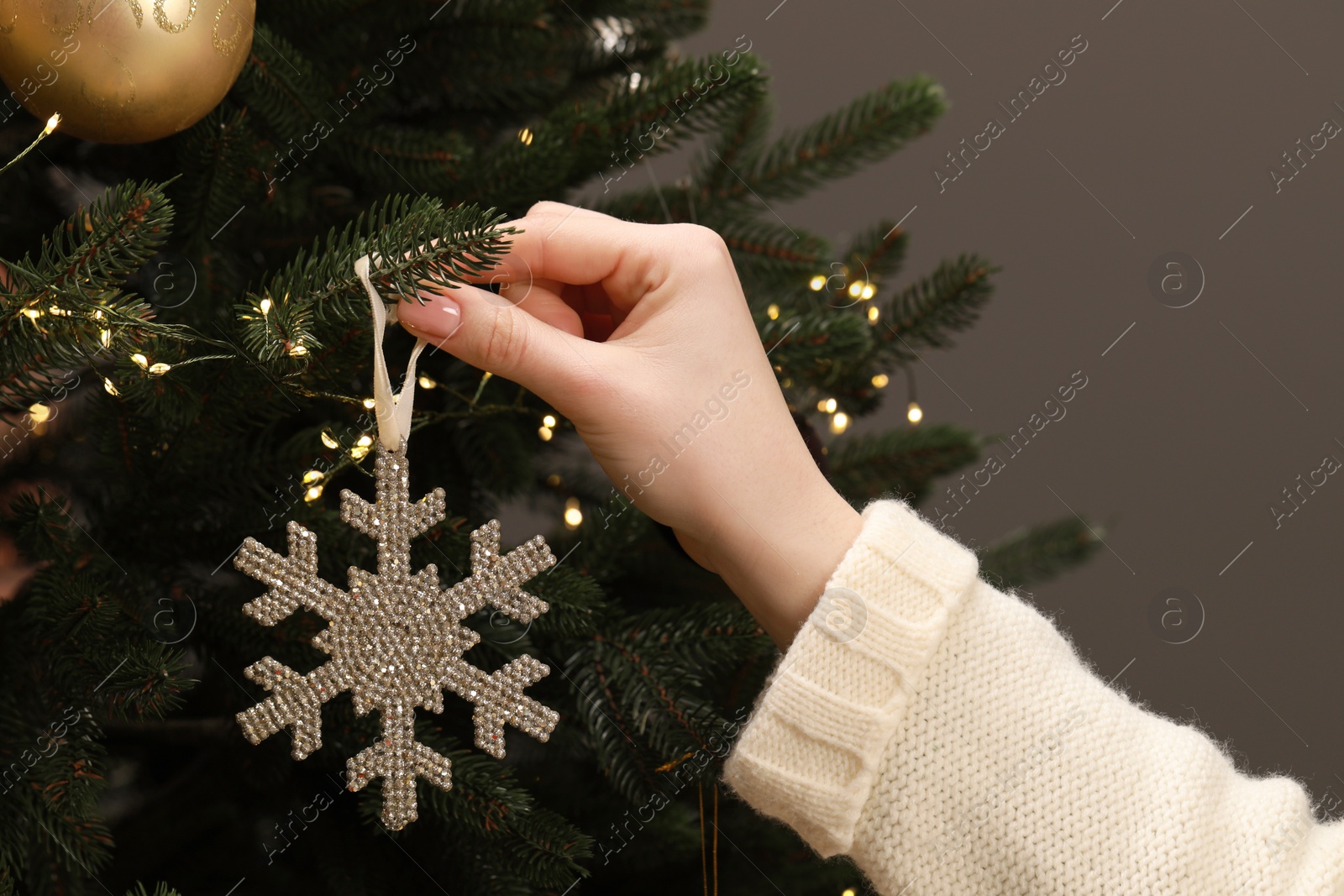 Photo of Woman decorating Christmas tree with beautiful bauble on grey background, closeup