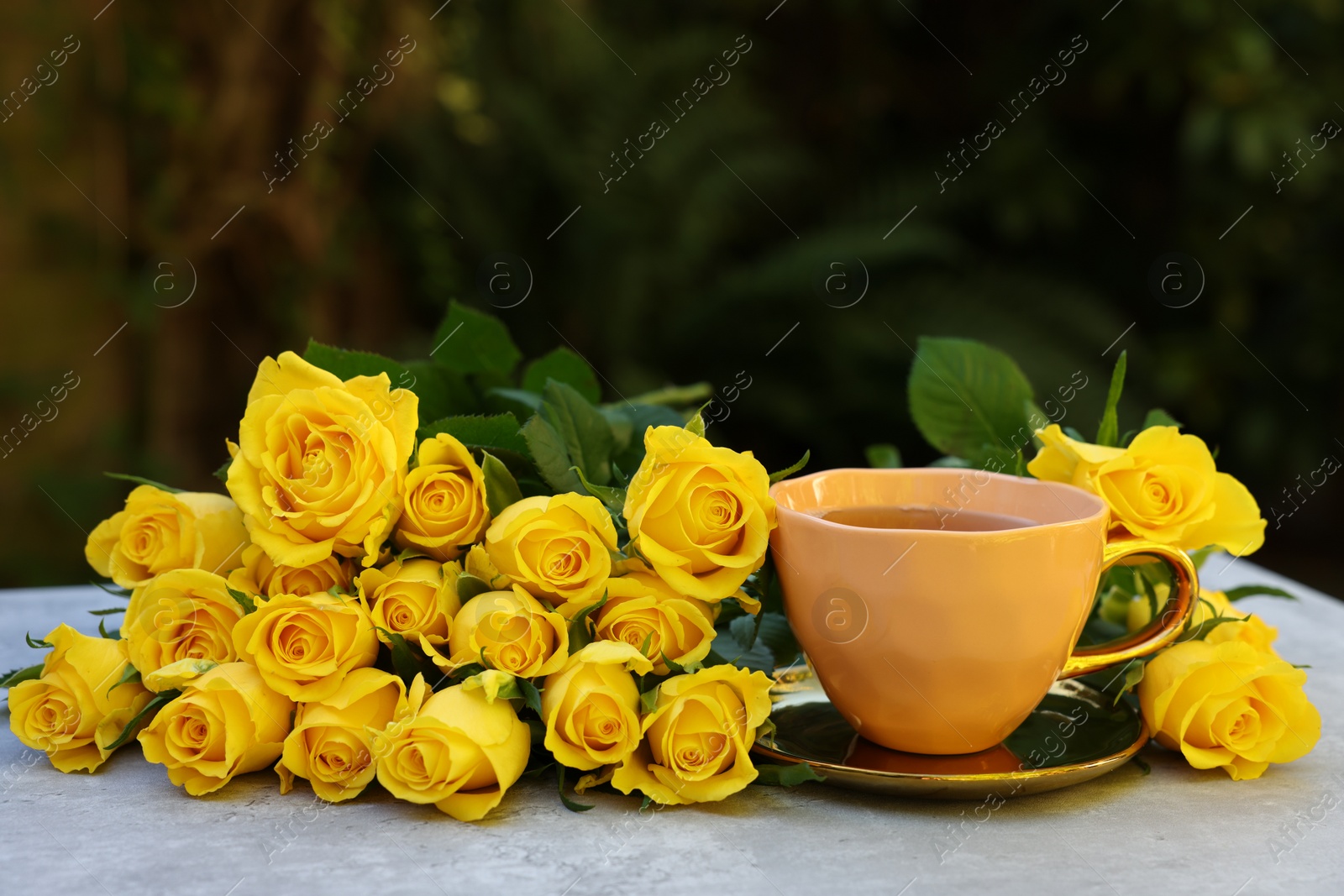 Photo of Cup of drink and beautiful yellow roses on light table outdoors, space for text