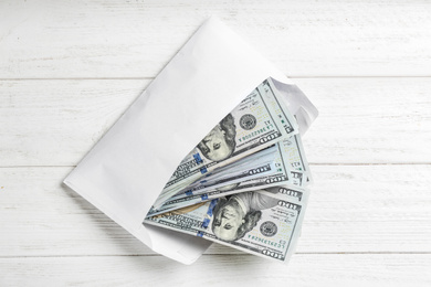 Envelope with dollar bills on white wooden table, top view. Bribe concept