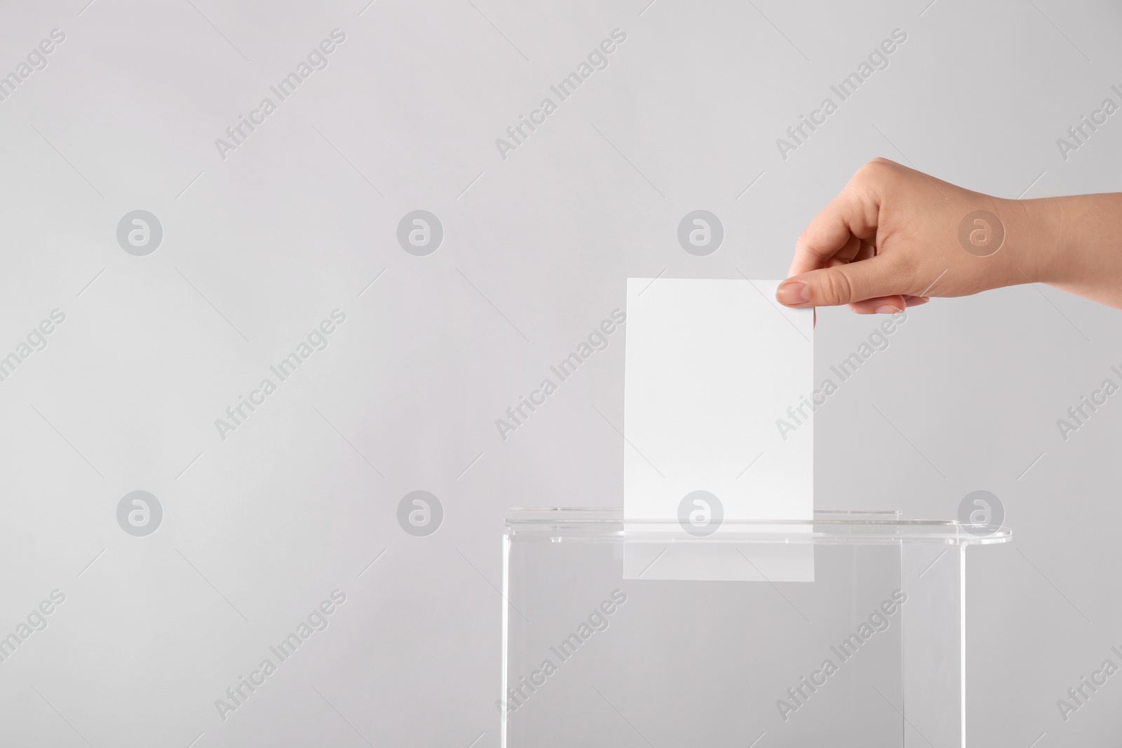 Photo of Woman putting her vote into ballot box on light grey background, closeup. Space for text