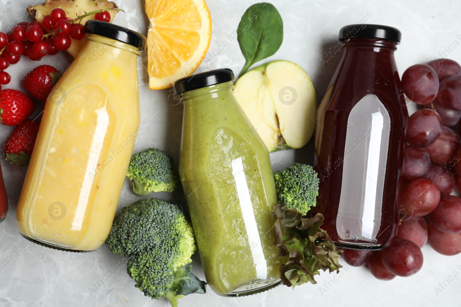 Photo of Bottles of delicious juices and fresh fruits on marble table, flat lay