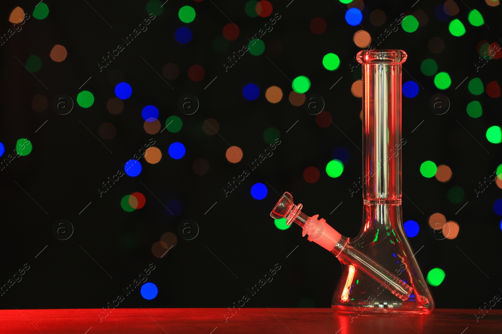 Photo of Glass bong against blurred lights, space for text. Smoking device