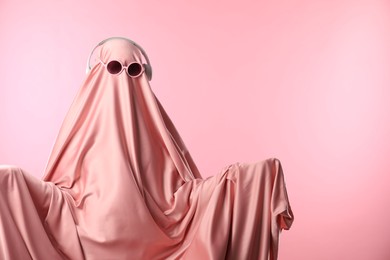 Glamorous ghost. Woman in sheet with sunglasses and headphones on pink background, space for text