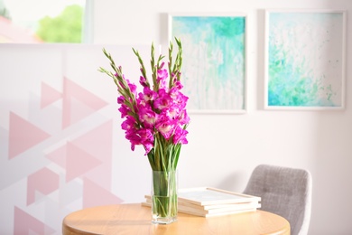 Vase with beautiful pink gladiolus flowers on wooden table in room, space for text