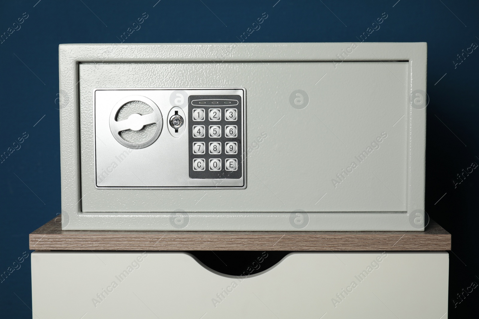 Photo of Steel safe with electronic lock on wooden table against blue background