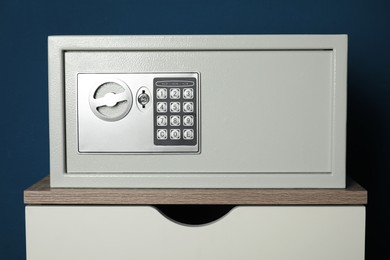 Steel safe with electronic lock on wooden table against blue background