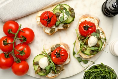 Photo of Tasty bruschettas with capers, vegetables and mozzarella served on white marble table, flat lay