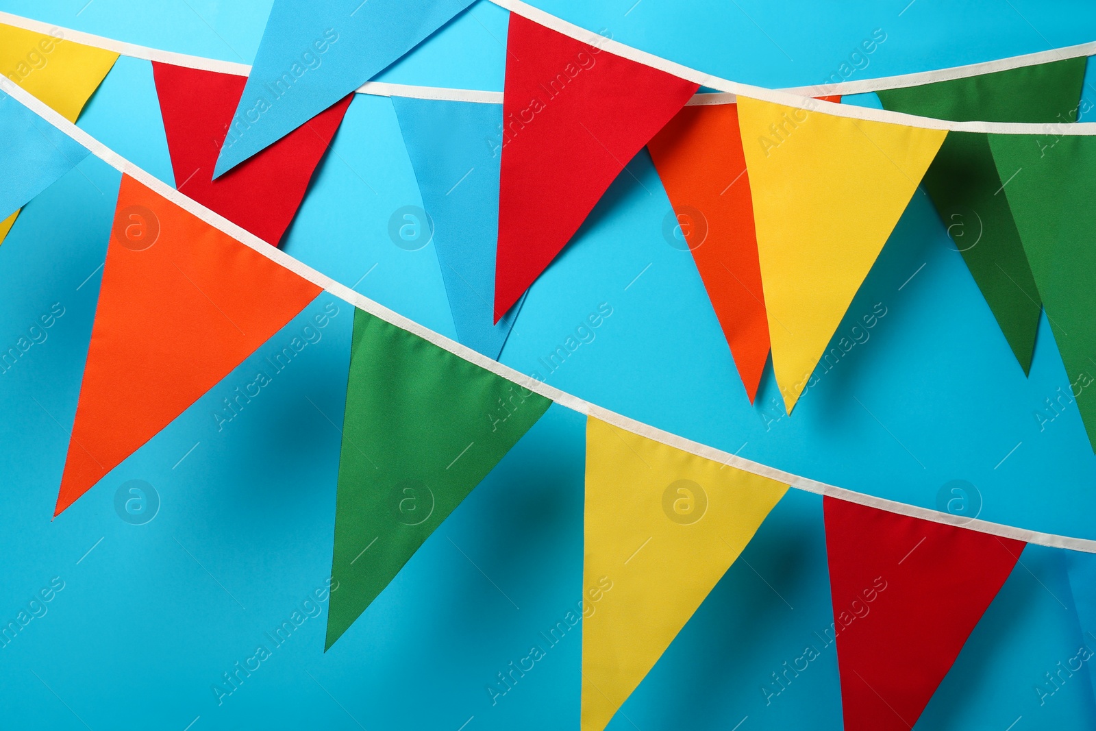 Photo of Buntings with colorful triangular flags hanging on light blue background. Festive decor