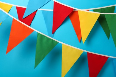 Buntings with colorful triangular flags hanging on light blue background. Festive decor
