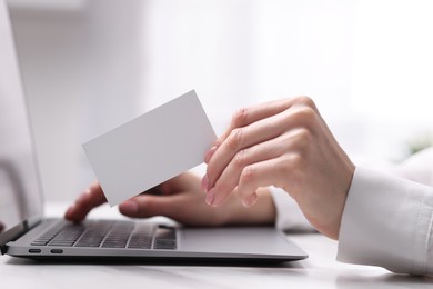 Woman with laptop holding blank business card at white table, closeup. Space for text