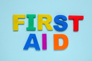 Photo of Words First Aid made of colorful letters on light blue background, flat lay