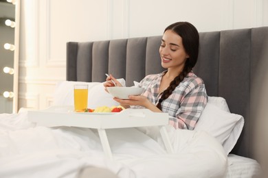 Happy young woman having breakfast on bed at home