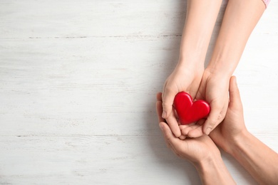 Photo of People holding red heart on wooden background, top view with space for text. Cardiology concept