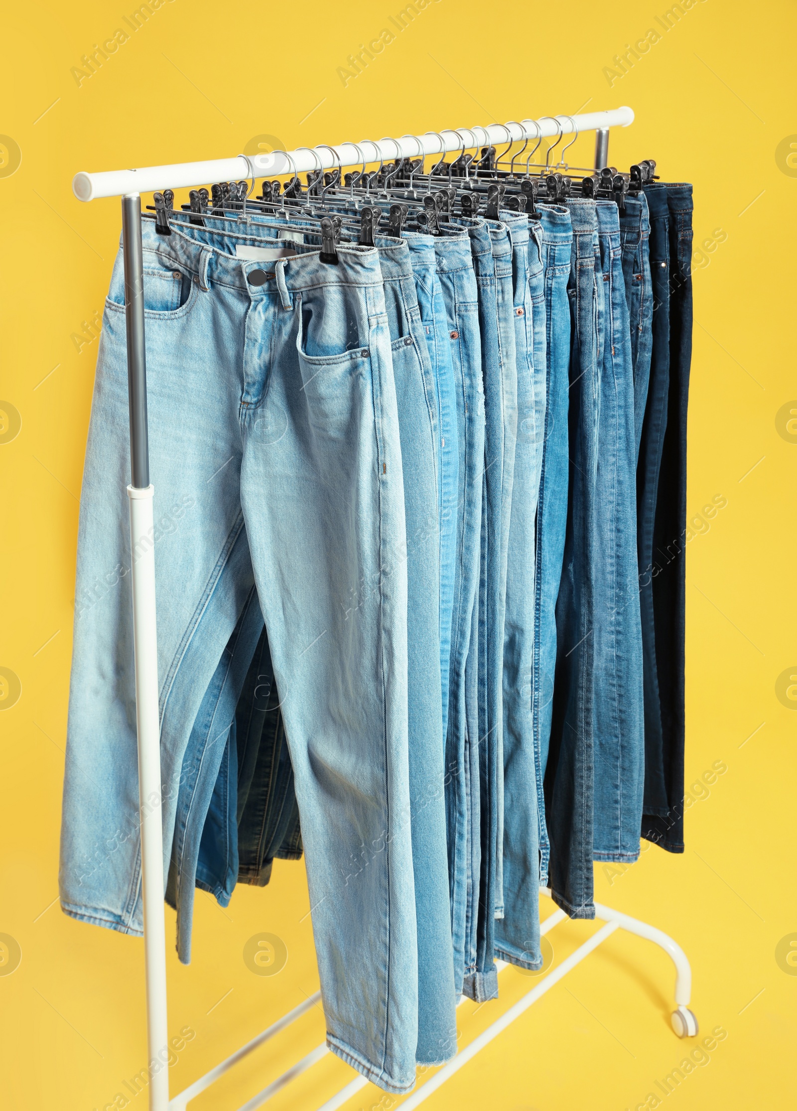 Photo of Rack with different jeans on yellow background