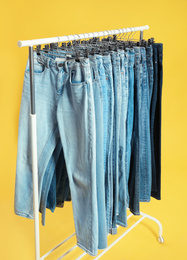 Rack with different jeans on yellow background