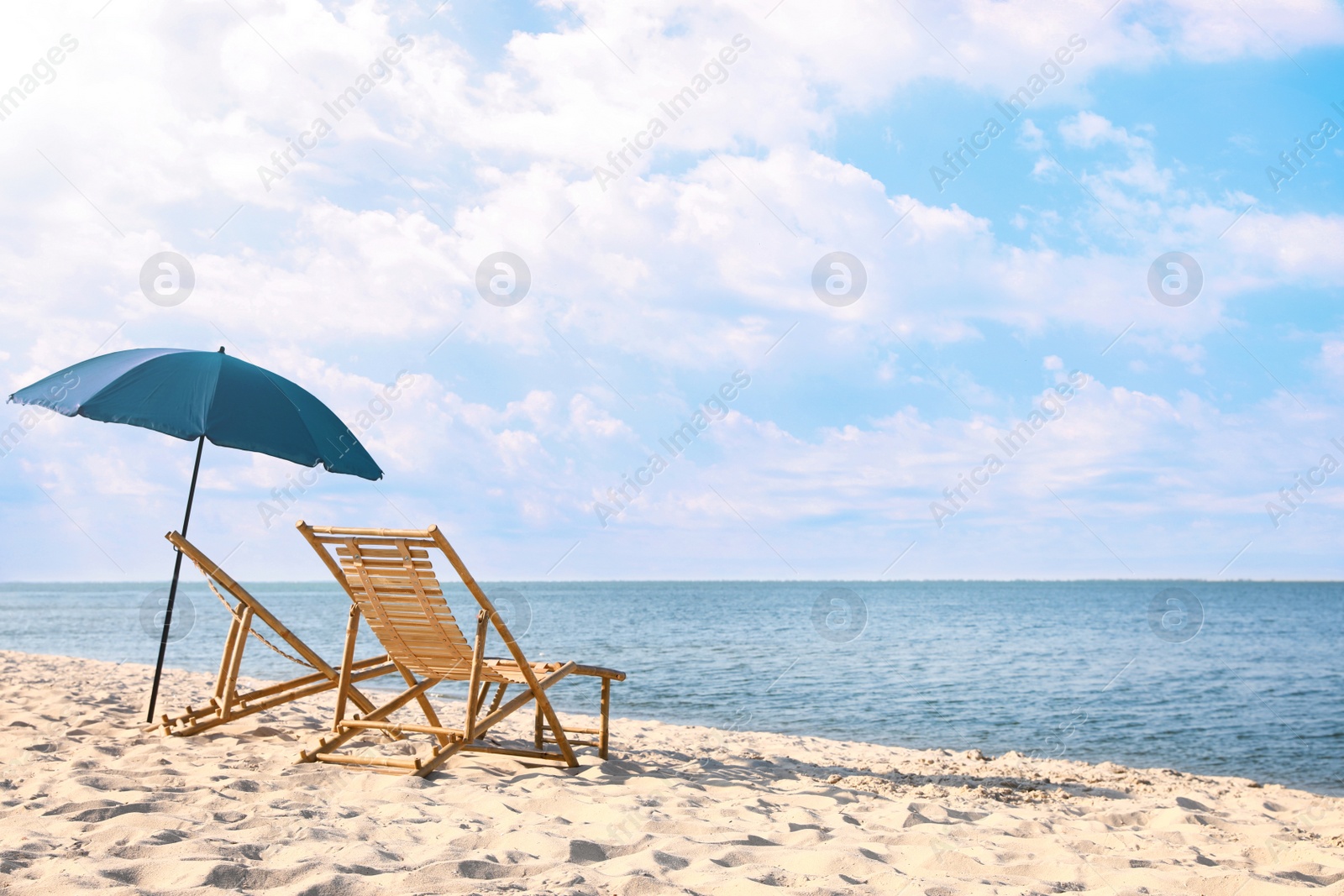 Photo of Empty wooden sunbeds and umbrella on sandy shore. Beach accessories