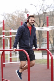 Young man with headphones listening to music and exercising on sports ground