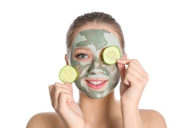 Beautiful woman with clay mask on her face holding cucumber slices against white background