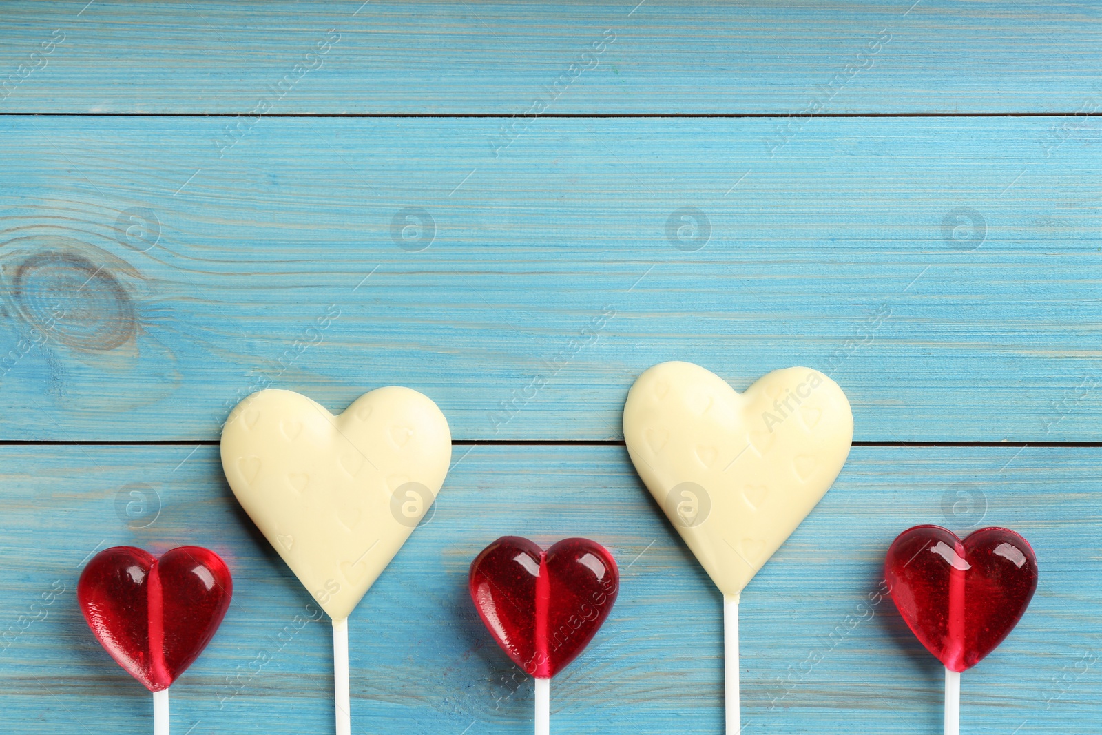 Photo of Heart shaped lollipops made of chocolate and sugar syrup on turquoise wooden table, flat lay. Space for text