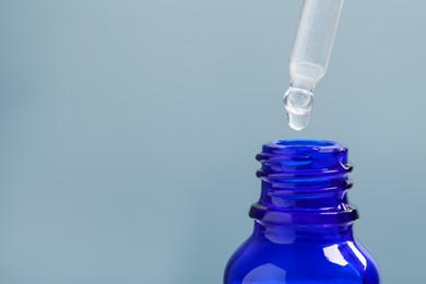 Dripping serum from pipette into bottle on grey background, closeup. Space for text