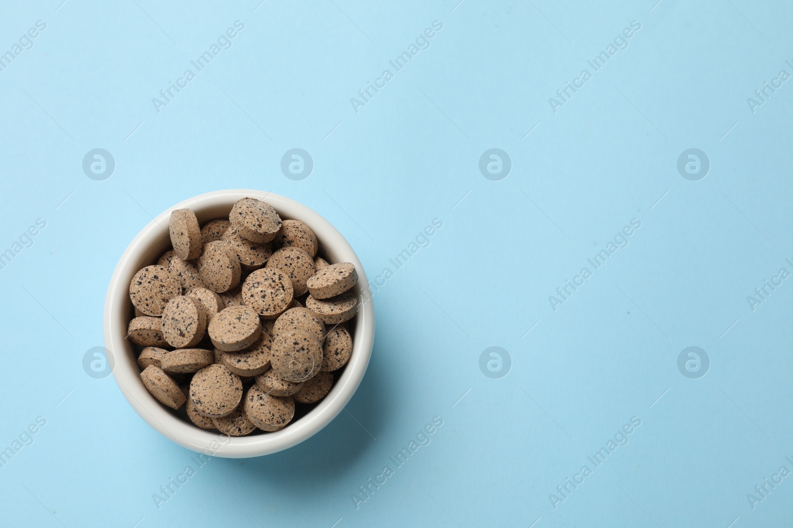 Photo of Vitamin pills in bowl on light blue background, top view. Space for text