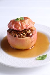 Photo of Tasty baked apple with nuts, honey and mint on white table, closeup